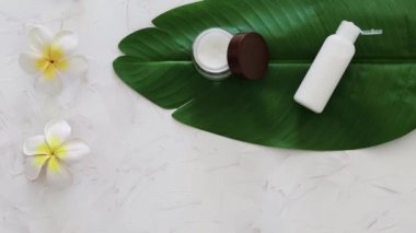 Sert kimyasallar içermeyen vejetaryen doğal güzellik, yüz kremi ve tropik yeşil yapraklı bir şişe vücut losyonu, monoi çiçekleri ve dikey çalışan kamera.