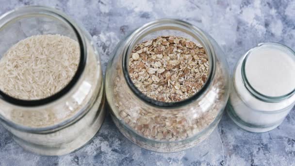 ビーガンパントリーのための健康的な非生鮮食品成分 オート麦粉と米とカメラのデフォルトとガラス瓶 — ストック動画