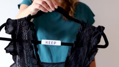 Düzenleme ve geri çevirme kavramsal natürmort, siyah beyaz üst ve metin etiketli elbise askıları tutan kadın onları tutmak ve Declutter arasında sınıflandırmak ve kameraya doğru yöneltmek ve sonra yukarı aşağı hareket ettirmek 