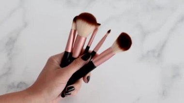 Güzellik endüstrisi ve kozmetik ürünleri, yüz ve göz makyajı için farklı makyaj fırçalarından oluşan el ele tutuşmalar ve nazikçe hareket eden