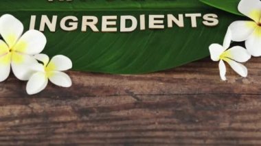 Güzellik endüstrisi ve etik vegan ürünler kavramsal natürmort, tropikal muz yaprağı üzerine monoi frangipani çiçekleri ve kamera dikey olarak dönük Doğal İçindekiler mesajı