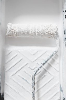 DIY ve ev geliştirme konsepti, üzerinde beyaz parlak boya ve boya rulosu olan boya tepsisinin yakın çekimi.