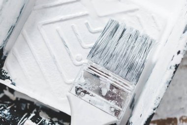 DIY ve ev geliştirme konsepti, üzerinde beyaz parlak boya ve boya fırçası olan boya tepsisinin yakın çekimi.