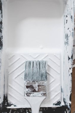 DIY ve ev geliştirme konsepti, üzerinde beyaz parlak boya ve boya fırçası olan boya tepsisinin yakın çekimi.