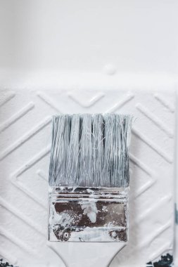 DIY ve ev geliştirme konsepti, üzerinde beyaz parlak boya ve boya fırçası olan boya tepsisinin yakın çekimi.