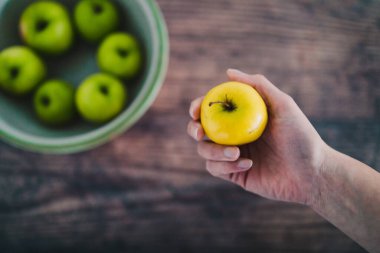 sağlıklı bitkisel gıda malzemeleri konsepti, bir kase yeşil elma ve yanında daha küçük sarı bir tane tutan el.