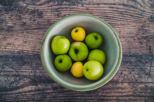 healthy plant-based food ingredients concept, bowl of green and yellow apples on wooden table