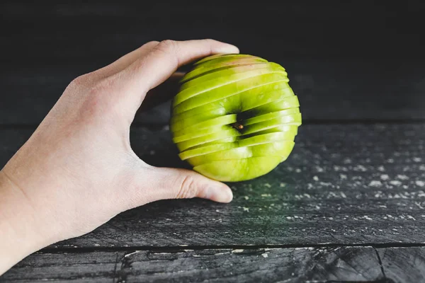 healthy plant-based food ingredients concept, hand holding green apple cut into thin equal slices stacked to maintain its original shape
