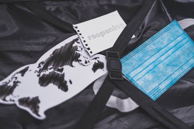 seyahat endüstrisi ve covid-19 sırasında uçmak, virüs koruması için cerrahi yüz maskeli valiz taşımak dünya haritasının yanında ve yeniden açılan bildiri