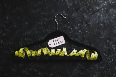 Moda endüstrisi ve etik ürünler konsepti, sarı şeritli kadife askı ve siyah arka planda Adil Ticaret etiketi