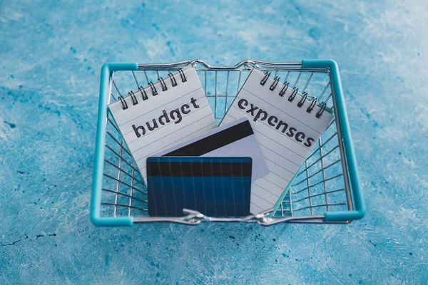 managing money and finance concept, budget and expenses notepads side by side on blue desk with shopping cart and credit cards