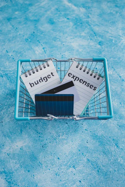 管理货币和财务概念 预算和支出笔记与购物车和信用卡并排放在蓝色桌子上 — 图库照片