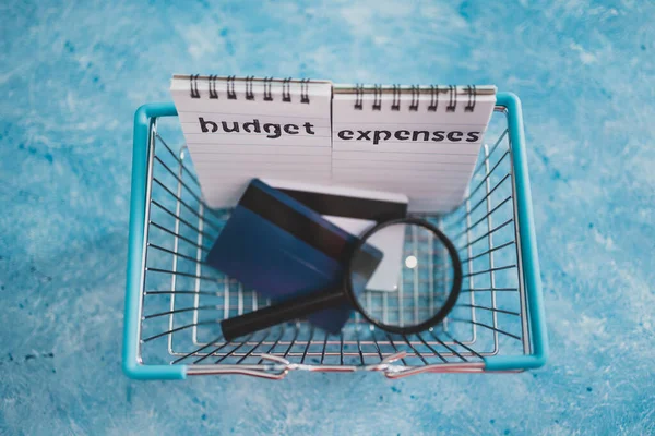 managing money and finance concept, budget and expenses notepads with shopping basket magnifying glass and credit cards on blue desk