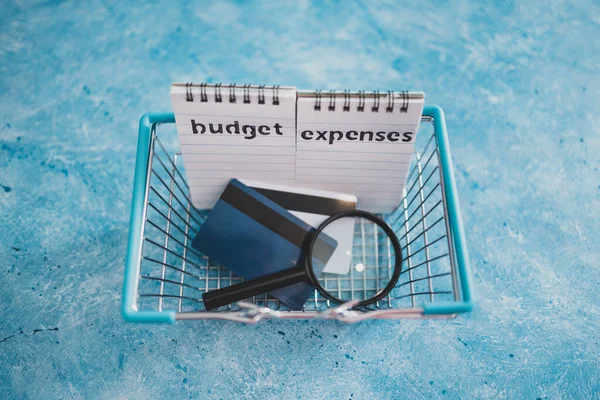 managing money and finance concept, budget and expenses notepads with shopping basket magnifying glass and credit cards on blue desk