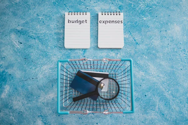 managing money and finance concept, budget and expenses notepads with shopping basket magnifying glass and credit cards on blue desk