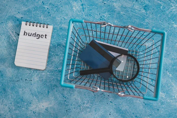 管理货币和财务概念 预算记事本蓝色桌子上装有购物篮放大镜和信用卡 — 图库照片