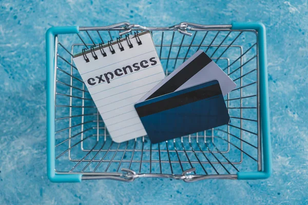 managing money and finance concept, expenses notepad inside shopping basket with credit cards on blue desk