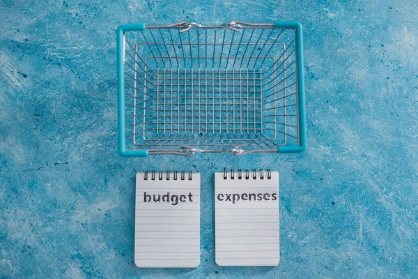 managing money and finance concept, budget and expenses notepads side by side on blue desk with shopping basket