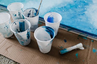Sanat ve zanaat hobileri konsepti, plastik bardaklarda renkleri olan mavi ve beyaz akrilik resim ve çalışma sürerken yanında da karışık boyama araçları