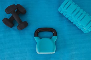 Ev jimnastik konsepti, kettlebell köpük silindirli mavi yoga minderi ve dambıllar yukarıdan aşağıya doğru atılmış.