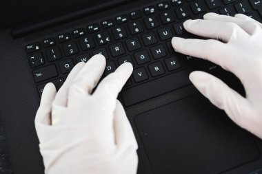ECOV-19 virüsü salgınından sonra yeni normaller, potansiyel olarak enfekte olmuş yüzeylerle temastan kaçınmak için iş yerinde paylaşılan bilgisayar klavyesine tek kullanımlık eldiven takan eller.