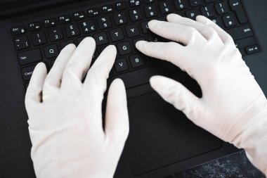 ECOV-19 virüsü salgınından sonra yeni normaller, potansiyel olarak enfekte olmuş yüzeylerle temastan kaçınmak için iş yerinde paylaşılan bilgisayar klavyesine tek kullanımlık eldiven takan eller.