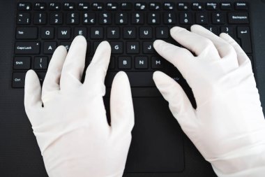 ECOV-19 virüsü salgınından sonra yeni normaller, potansiyel olarak enfekte olmuş yüzeylerle temastan kaçınmak için iş yerinde paylaşılan bilgisayar klavyesine tek kullanımlık eldiven takan eller.