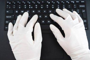 ECOV-19 virüsü salgınından sonra yeni normaller, potansiyel olarak enfekte olmuş yüzeylerle temastan kaçınmak için iş yerinde paylaşılan bilgisayar klavyesine tek kullanımlık eldiven takan eller.