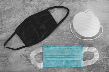 Covid-19 virüs salgınından sonraki yeni normal. Beton yüzeyde cerrahi maske, kumaş ve inşaat maskeleri de dahil olmak üzere farklı yüz maskeleri.