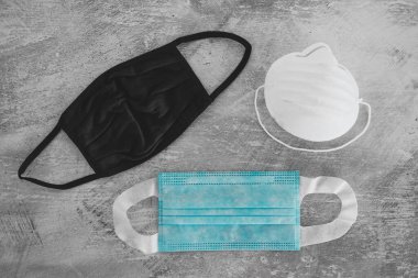 Covid-19 virüs salgınından sonraki yeni normal. Beton yüzeyde cerrahi maske, kumaş ve inşaat maskeleri de dahil olmak üzere farklı yüz maskeleri.
