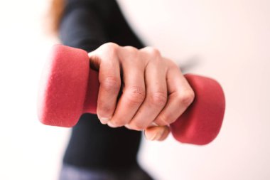 Evde fitness ve internet koçluğu konsepti, spor kıyafetleri içindeki kadının elinde dambıl ve akıllı telefon tutarak spor videosu ya da internetteki rutini takip etmesi.