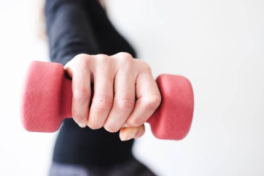 Spor elbiseli bir kadın, dambıl tutuyor ve vücudunun üst kısmını çalıştırıyor.