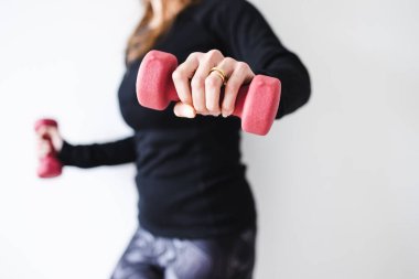 Spor elbiseli bir kadın, dambıl tutuyor ve vücudunun üst kısmını çalıştırıyor.