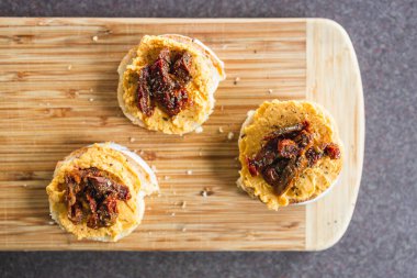 sağlıklı bitkisel yemek tarifleri konsepti, kırmızı biber humuslu vejetaryen aperatifi üzerine dilimlenmiş baget ekmeği, üstüne de kurutulmuş domates.