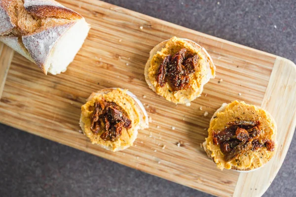 sağlıklı bitkisel yemek tarifleri konsepti, kırmızı biber humuslu vejetaryen aperatifi üzerine dilimlenmiş baget ekmeği, üstüne de kurutulmuş domates.