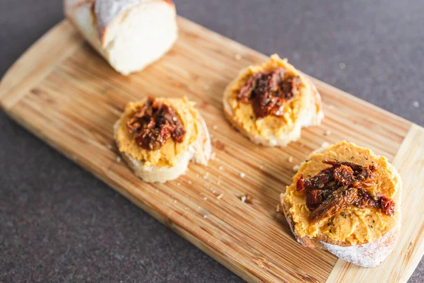 sağlıklı bitkisel yemek tarifleri konsepti, kırmızı biber humuslu vejetaryen aperatifi üzerine dilimlenmiş baget ekmeği, üstüne de kurutulmuş domates.