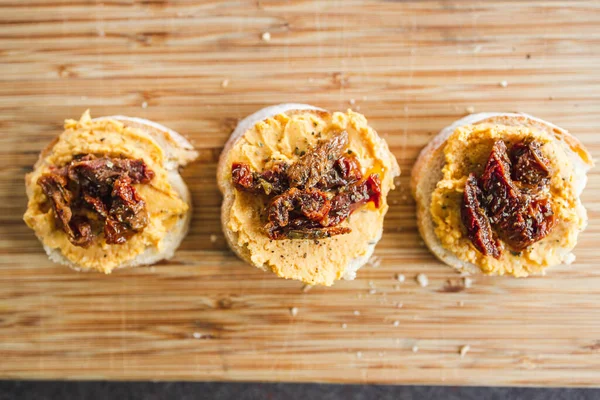 sağlıklı bitkisel yemek tarifleri konsepti, kırmızı biber humuslu vejetaryen aperatifi üzerine dilimlenmiş baget ekmeği, üstüne de kurutulmuş domates.