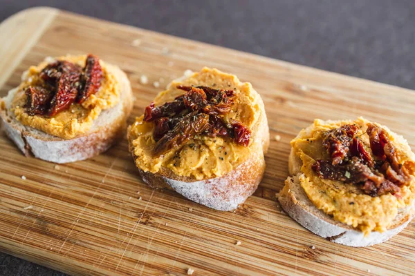 sağlıklı bitkisel yemek tarifleri konsepti, kırmızı biber humuslu vejetaryen aperatifi üzerine dilimlenmiş baget ekmeği, üstüne de kurutulmuş domates.