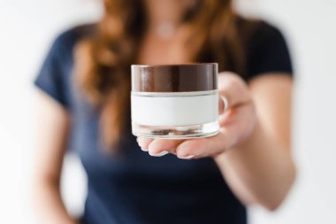 Kameranın önünde elinde nemlendirici kavanozu tutan bir kız sığ alan derinliğinde çekilen ürünü, güzellik blogcuları ve etkilenenlerin ürünleri yeniden yönetmesi veya çevrimiçi makyaj dersleri vermesi kavramını gösteriyor., 