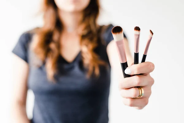girl holding make-up brushes in front of the camera showing the product shot at shallow depth of field, concept of beauty bloggers and influencers recommanding products or making online make-up tutorials,