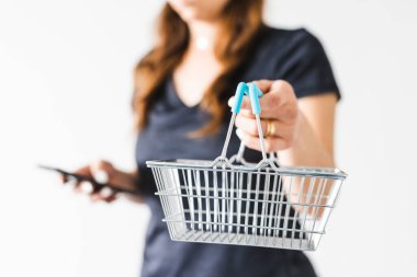 Satın almadan önce pazarlama ve ürün değerlendirmesi yapma, alışveriş sepetini kameraya doğru tutan ve akıllı telefonunu kontrol ederek ne alacağına karar veren kadın.