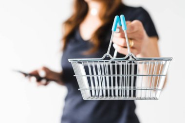 Satın almadan önce pazarlama ve ürün değerlendirmesi yapma, alışveriş sepetini kameraya doğru tutan ve akıllı telefonunu kontrol ederek ne alacağına karar veren kadın.