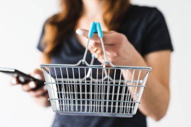 Satın almadan önce pazarlama ve ürün değerlendirmesi yapma, alışveriş sepetini kameraya doğru tutan ve akıllı telefonunu kontrol ederek ne alacağına karar veren kadın.