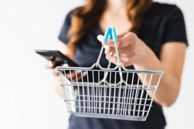 Satın almadan önce pazarlama ve ürün değerlendirmesi yapma, alışveriş sepetini kameraya doğru tutan ve akıllı telefonunu kontrol ederek ne alacağına karar veren kadın.