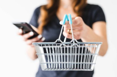 Satın almadan önce pazarlama ve ürün değerlendirmesi yapma, alışveriş sepetini kameraya doğru tutan ve akıllı telefonunu kontrol ederek ne alacağına karar veren kadın.