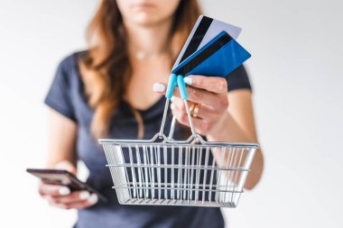 Satın almadan önce pazarlama ve ürün değerlendirmesi yapma kavramı, kredi kartlarıyla alışveriş sepetini kameraya doğru tutan ve akıllı telefonuyla ne alacağına karar veren kadın.