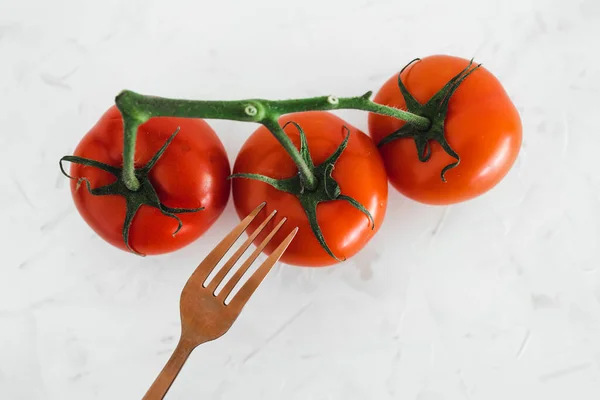 simple ingredients and whole food diet concept, close-up of three tomatoes on vine with fork next to them on white minimalist background