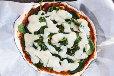 Sağlıklı bitkisel yemek tarifleri konsepti, kaju peynirli vegan pizza ve fırına girmek üzere olan ıspanak.