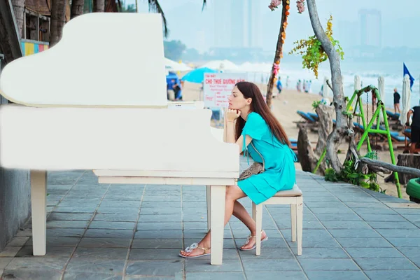 一个女孩坐在海滩上的钢琴旁边 — 图库照片