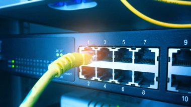 Ağ anahtarı ve ethernet kablosu raf dolabının arka planında.